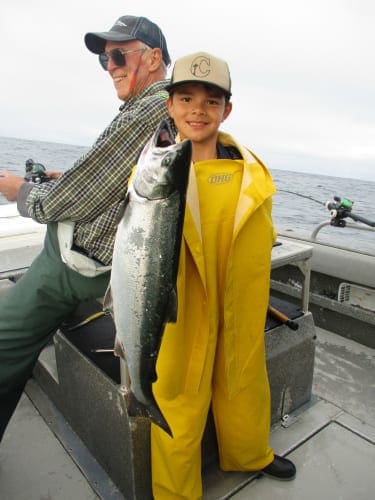 young boy in waders holding small silver salmon on fishing boat