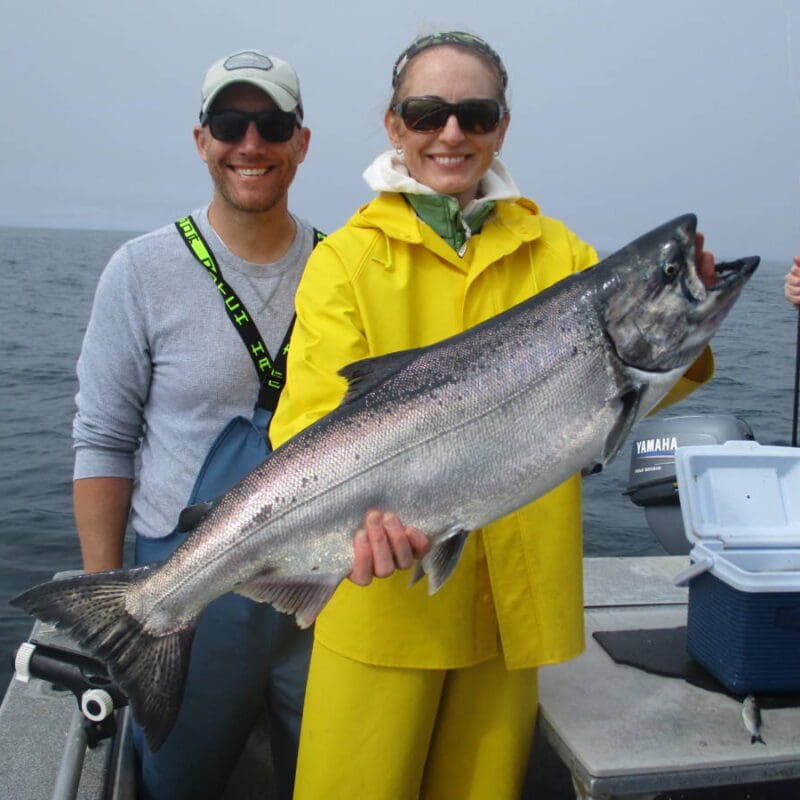 woman in yellow slickers holding large king salmon on boat