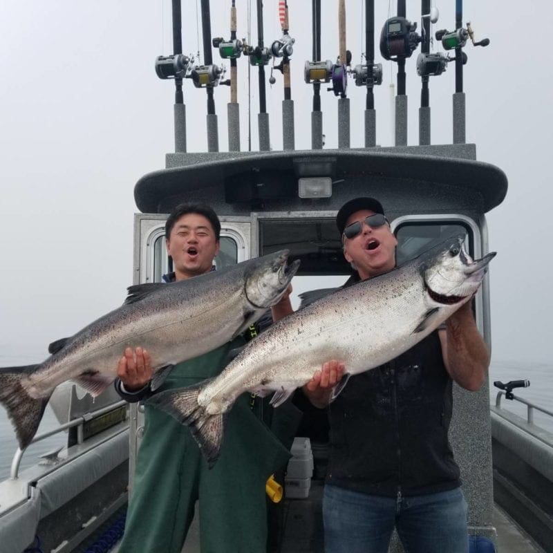 Two men stand on an Angling Unlimited boat holding salmon
