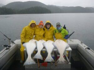 4 people sitting behind 4 halibut on boat stern