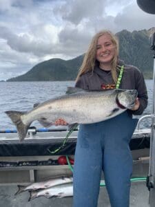 young blonde woman holding a large king salmon on boat
