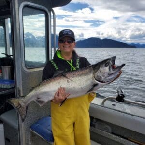 woman in yellow slickers holding large king salmon on boat
