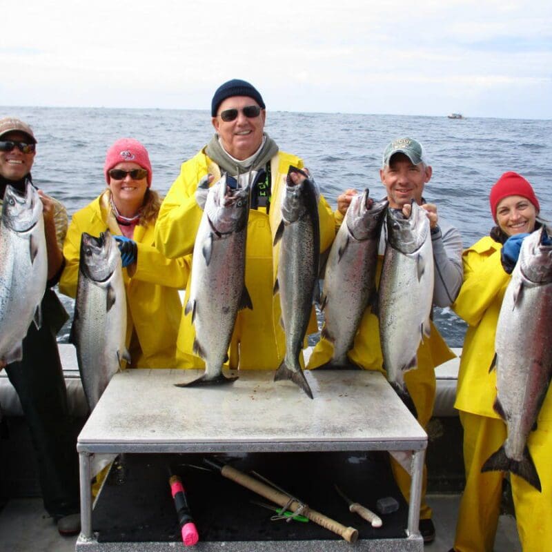 group of people holding salmon at back of boat
