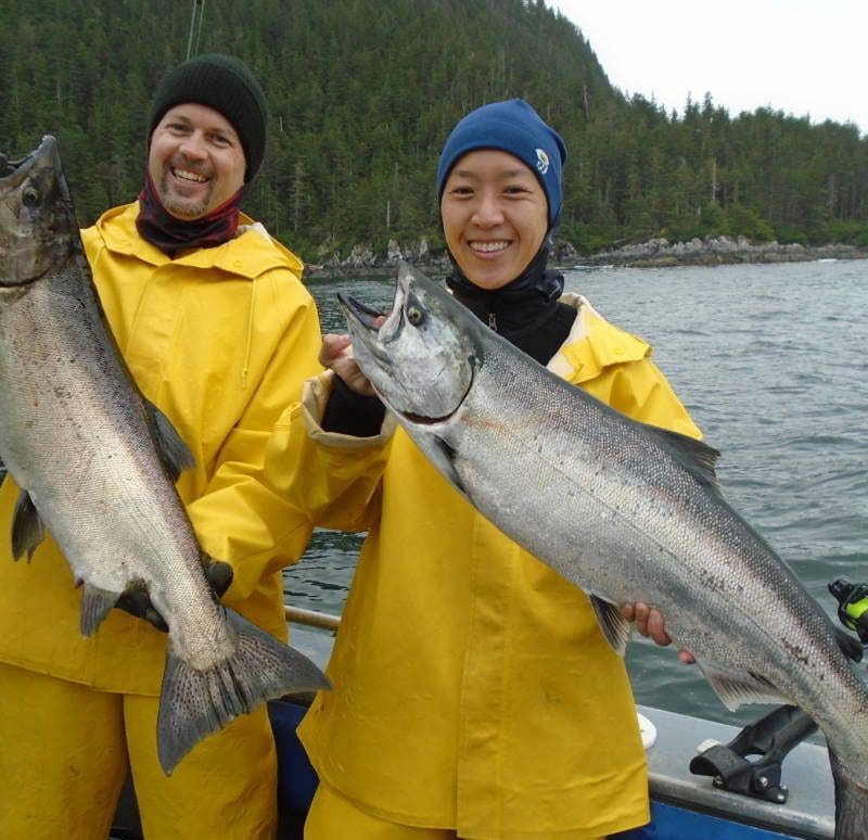 2 people in yellow slickers and hats holding large king salmon