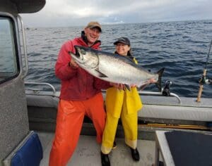 man and woman holding large salmon on fishing boat