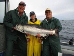 2 men and a woman in hats holding large salmon on boat