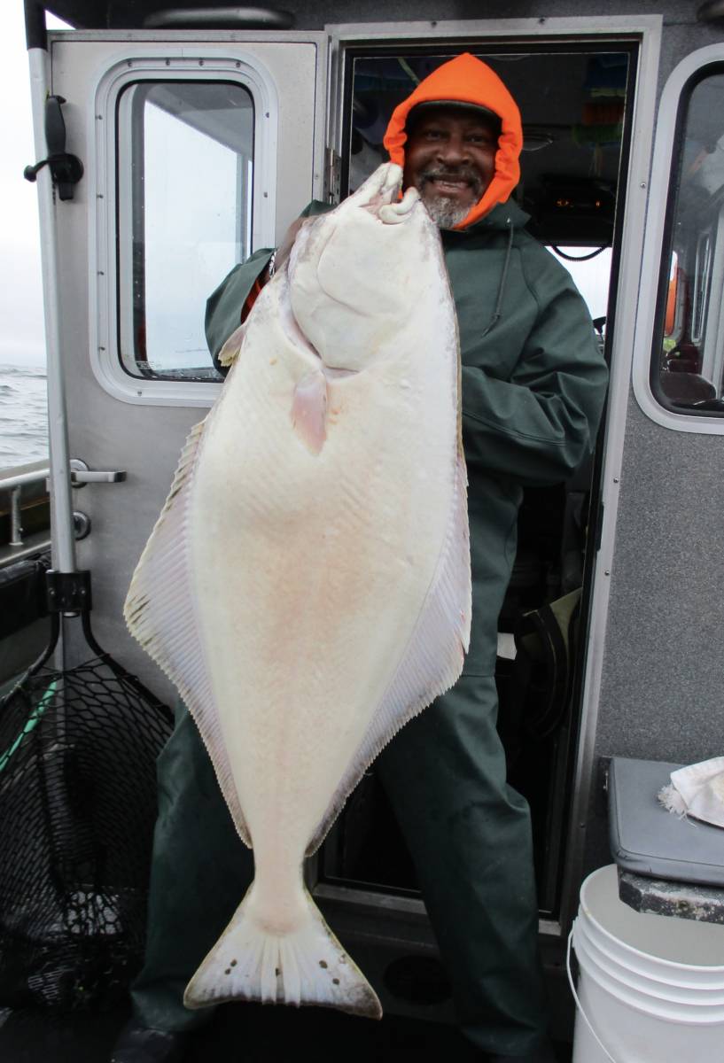 man standing up on boat holding large halibut