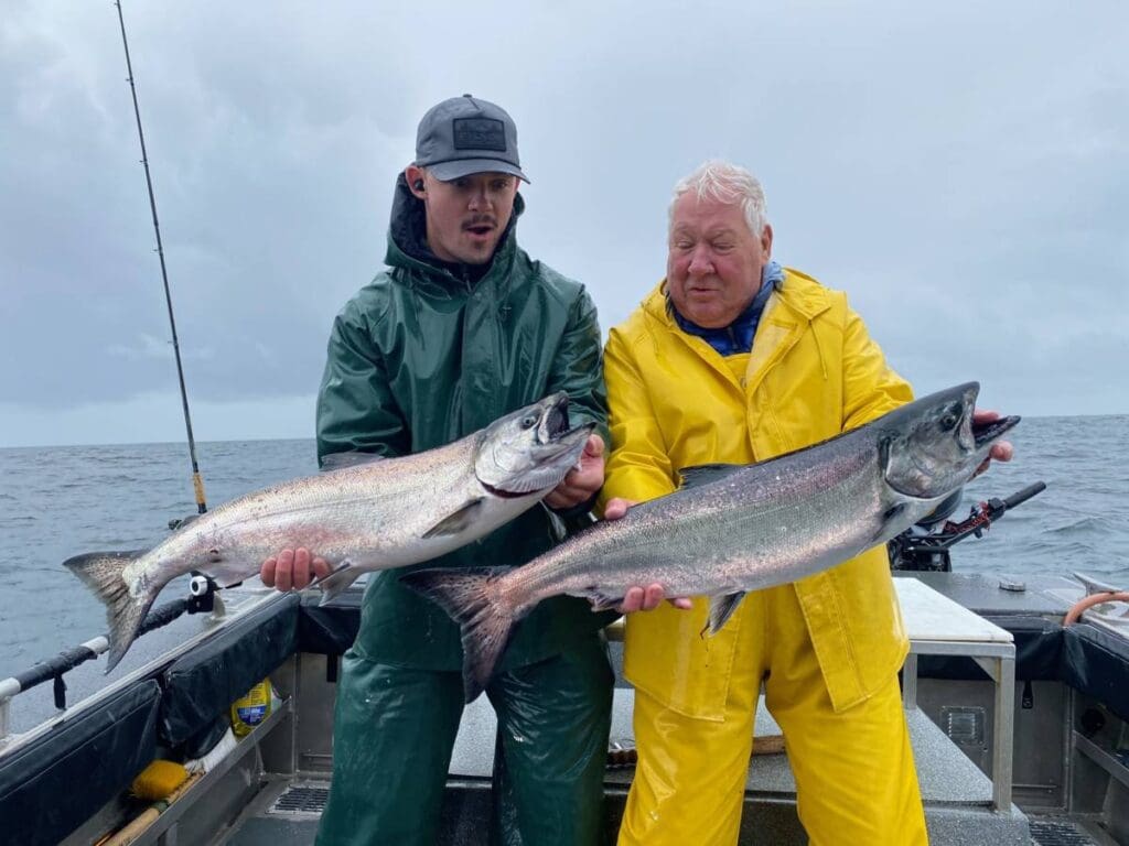 Two men, one in green and one in yellow, admire their king salmon catches on a charter boat