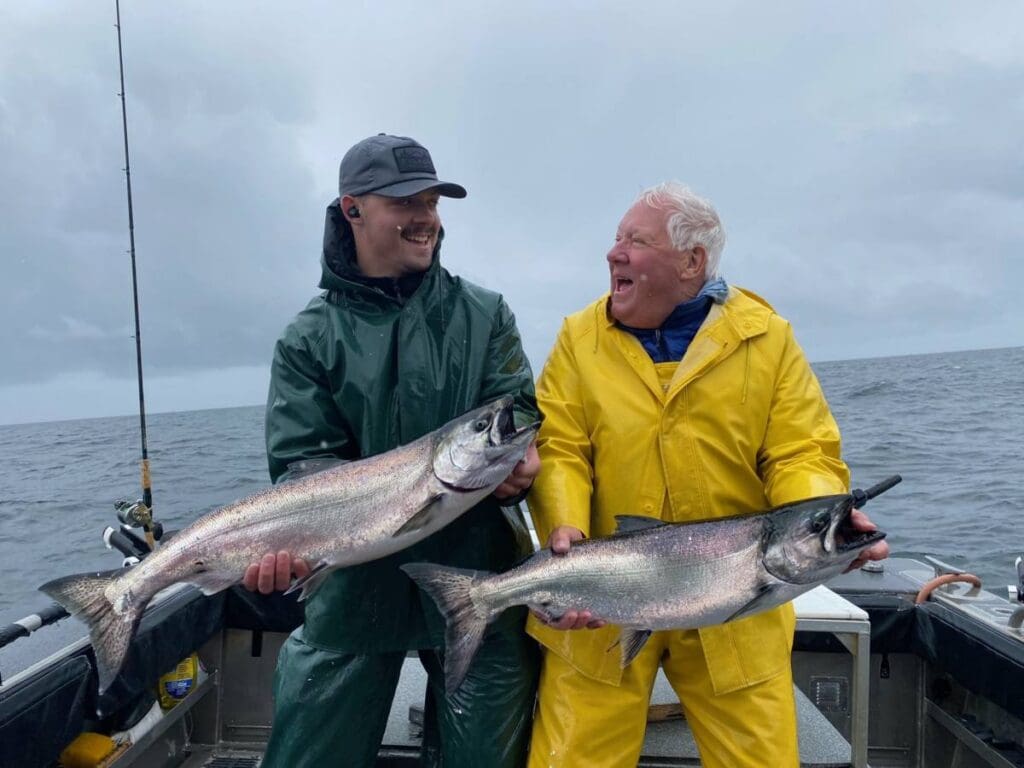 Two men laughing as they showcase their giant king salmon catches on the boat