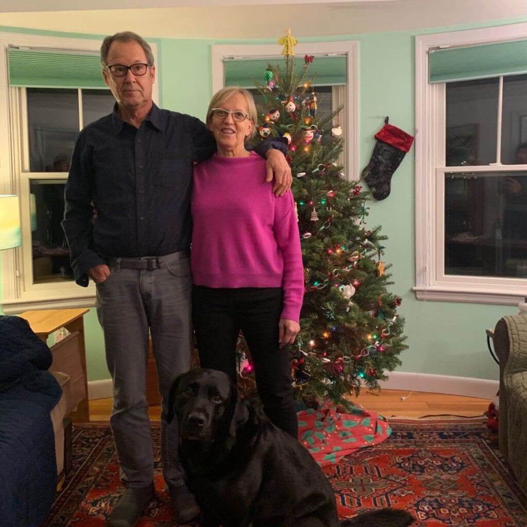 Couple stands in front of a christmas tree with a black dog