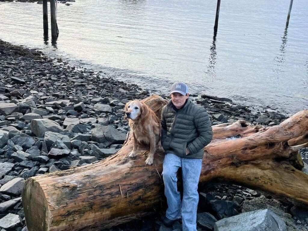 Man sits on washed up stump with golden retriever