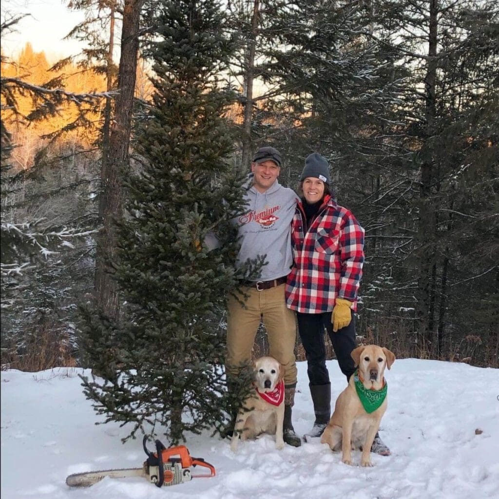 Couple stands outside with a christmas tree and their dogs
