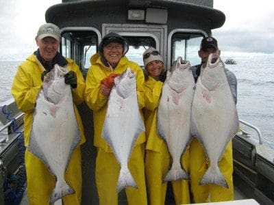 Four Angling Unlimited guests pose with halibut on a boat