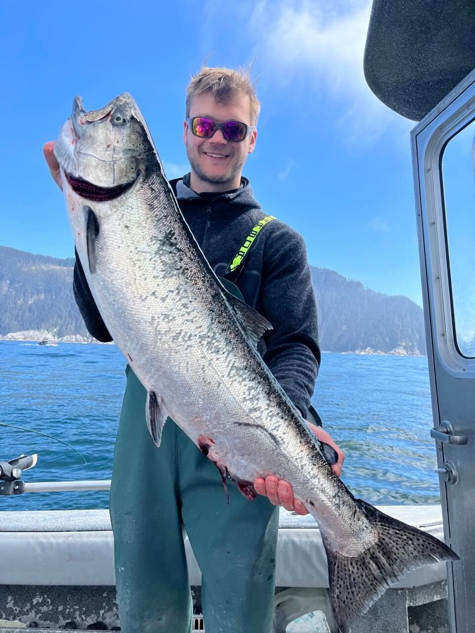 A man on a boat in Sitka, Alaska poses holding a large salmon
