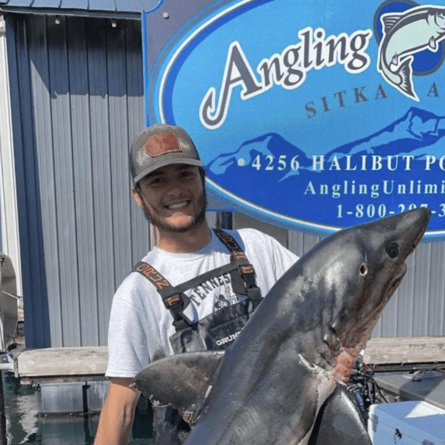 Angling Unlimited crew member, Logan Bielke, holds a large salmon shark in Sitka, Alaska