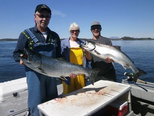 Three people stand with two of them holding king salmon in Sitka, Alaska