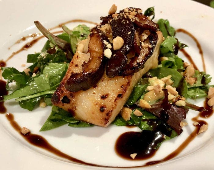 Baked alaskan black cod plated on leafy greens on a plate with a brown sauce