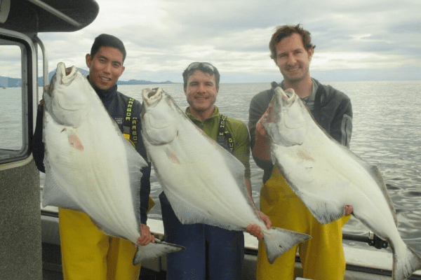 Three men stand on a boat holding halibut in Sitka, Alaska