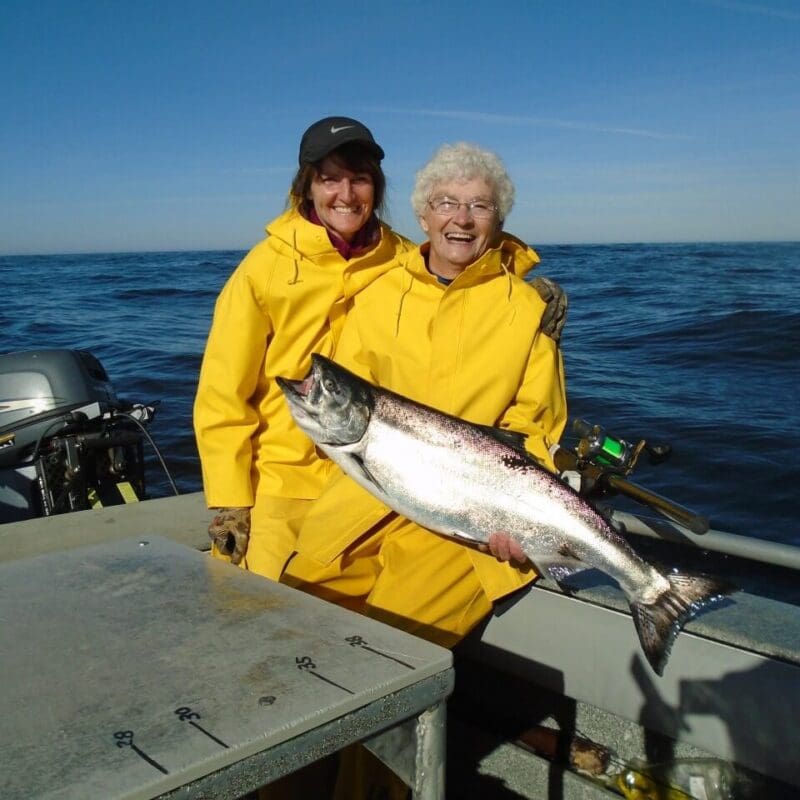 Two women in yellow hold up a salmon in Sitka, Alaska